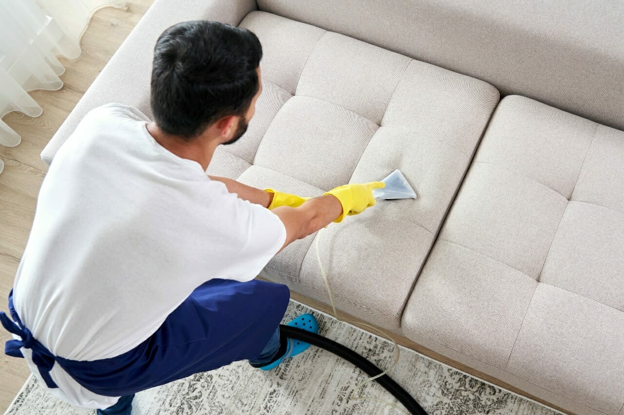 close-up-of-housekeeper-holding-modern-washing-vacuum-cleaner-and-cleaning-dirty-sofa-with-professionally-detergent-professional-springclean-at-home-concept