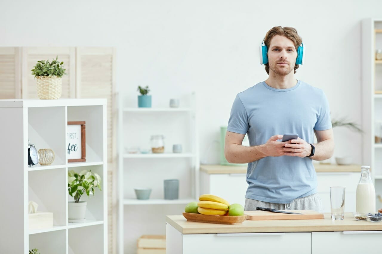 portrait-of-young-man-wearing-headphones-and-listening-to-music-on-the-phone-while-cooking-in-the-kitchen
