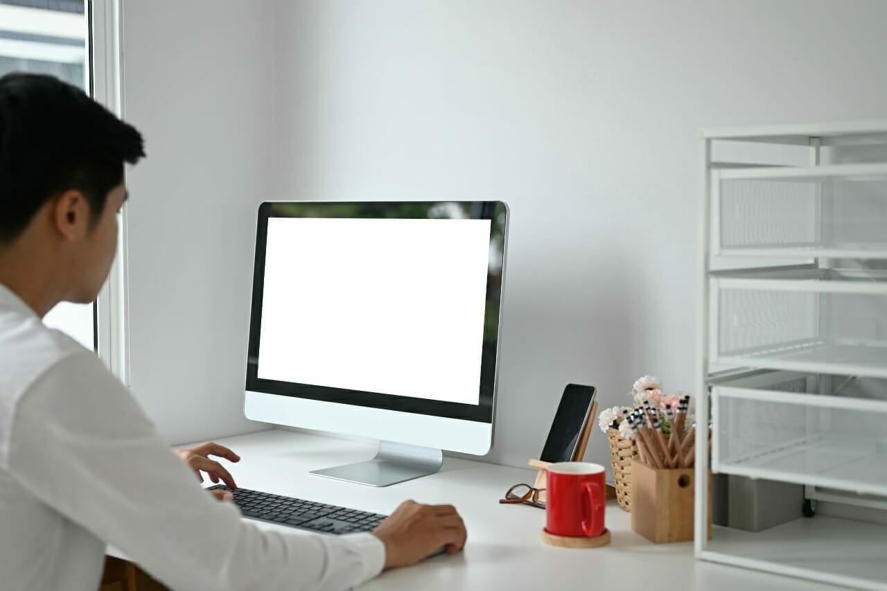 young-man-working-with-computer-pc-at-home-office-and-empty-screen-display