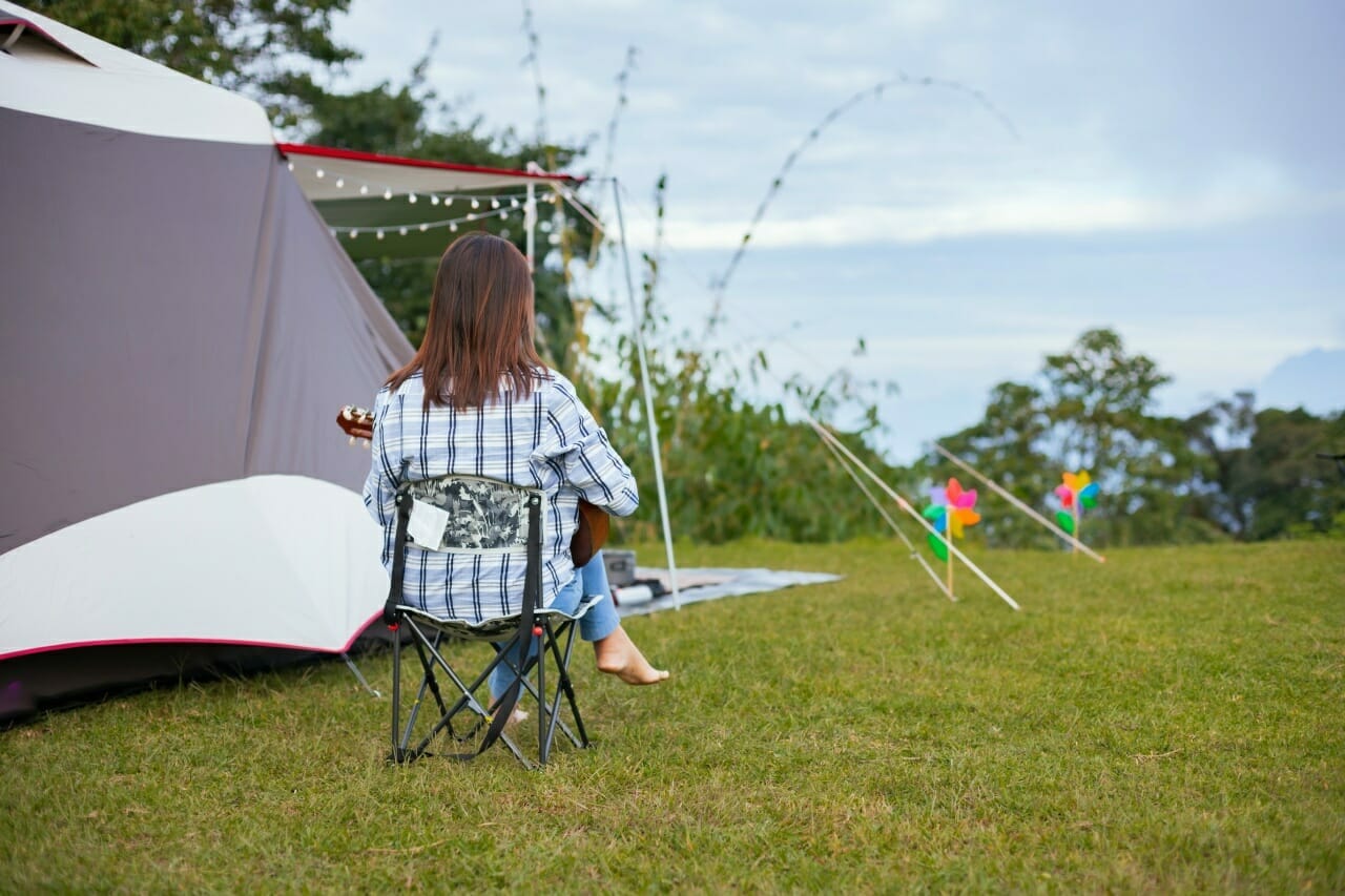 asian-woman-sitting-picnic-chair-playing-guitar-while-camping-with-family-camping-site-beautiful-nature
