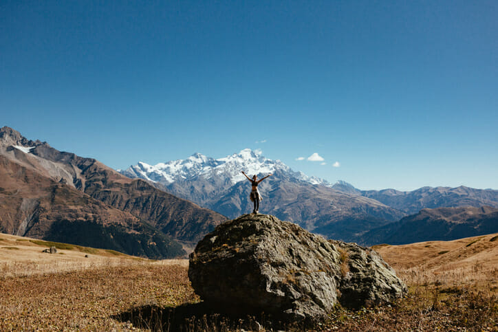 Woman enjoying the amazing view high up in the mountains raising her hands up